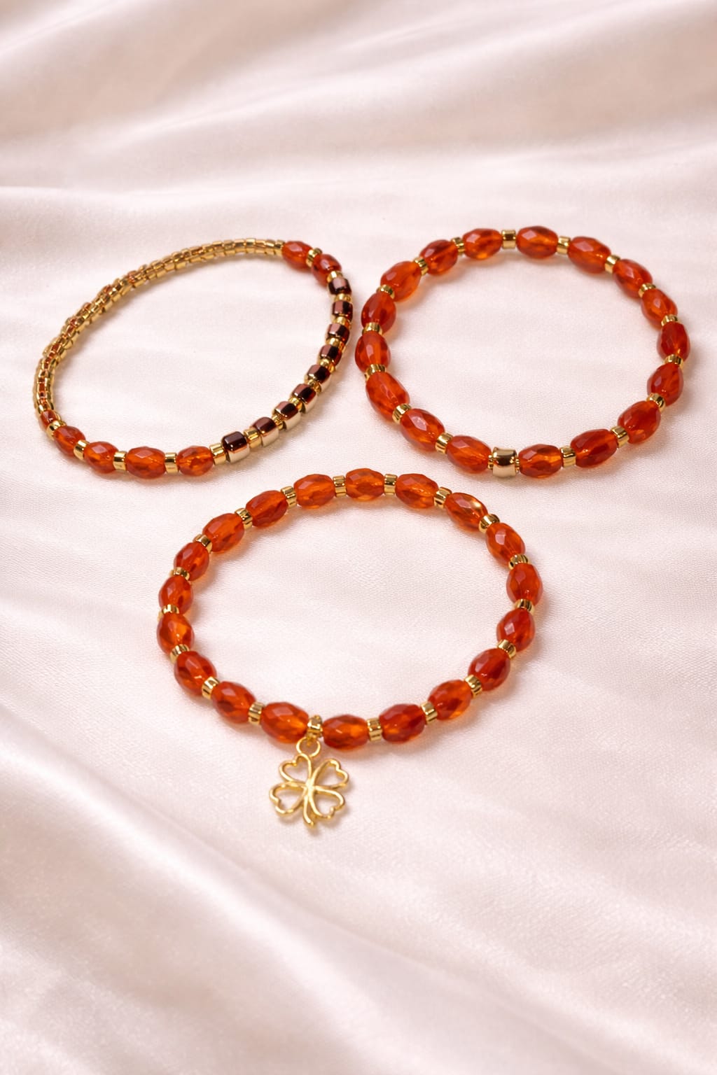Set of three orange and gold stretch bracelets with gold clover charm